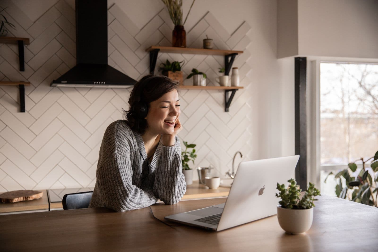 A woman laughing during a video call at her kitchen table